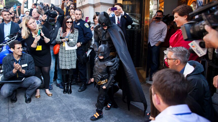 BatKid and Batman leave a former bank after arresting the Riddler