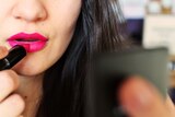 A woman puts on lipstick in a close-up image