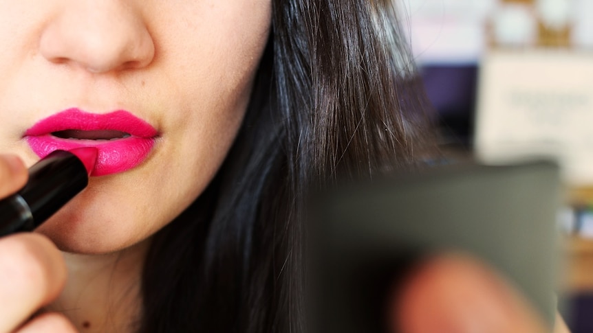 A woman puts on lipstick.