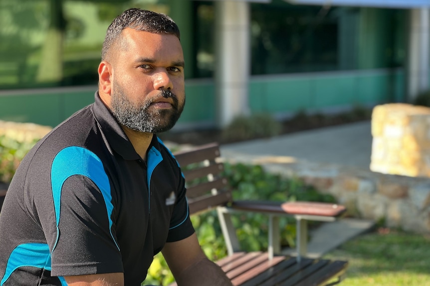 A man wearing a black polo shirt standing in a garden