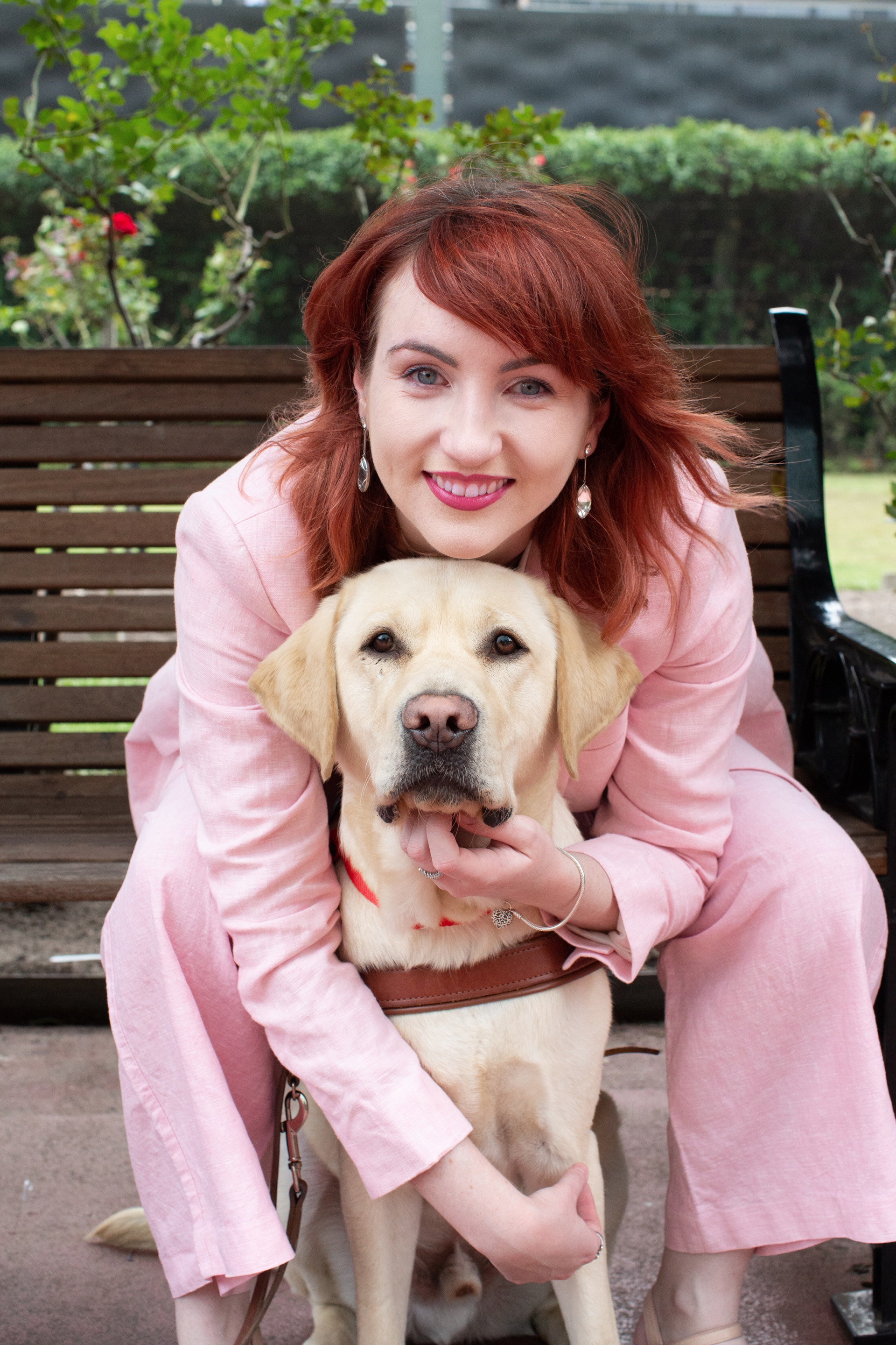 Ingrid wears a pink suit and sits on a bench. She leans to hug her dog Banner who is seated in front of her, facing the camera, Ausnew Home Care, NDIS registered provider, disability