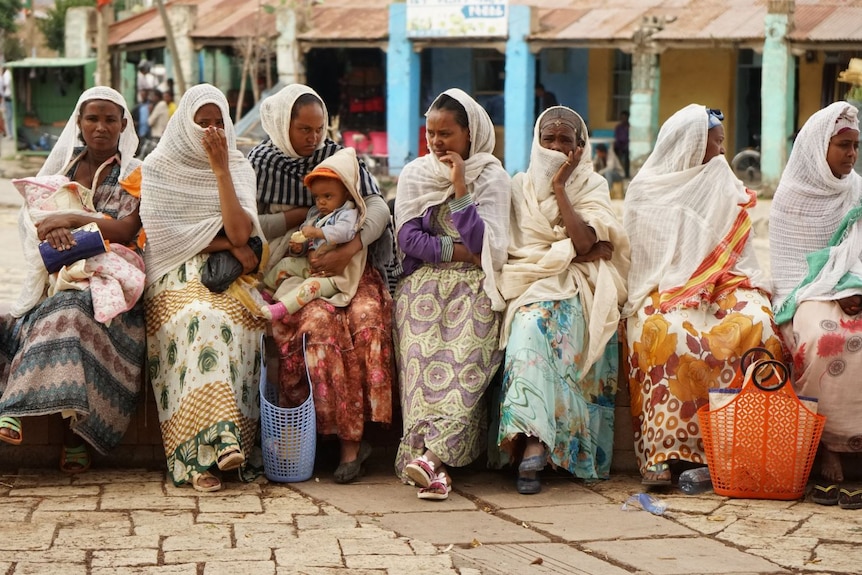 A group of women sitting in a line along a wall.