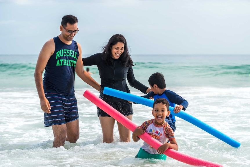 A mother and father play with her sons in the surf at Mooloolaba Beach.