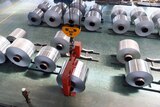 A birds-eye image of a worker in an aluminium factory lifting up a large roll of aluminium foil with an electronic winch