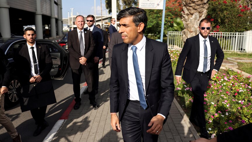 British Prime Minister Rishi Sunak walks with entourage of security. 