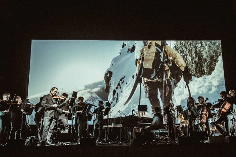 The Australian Chamber Orchestra on a stage with the documentary film Mountain in the background.
