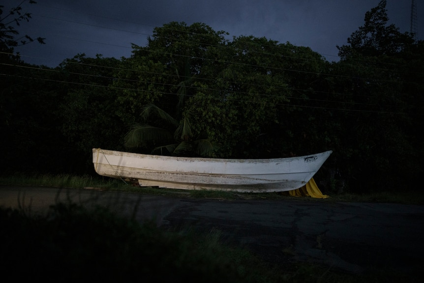 A white wooden boat is pictured on shore at dusk.