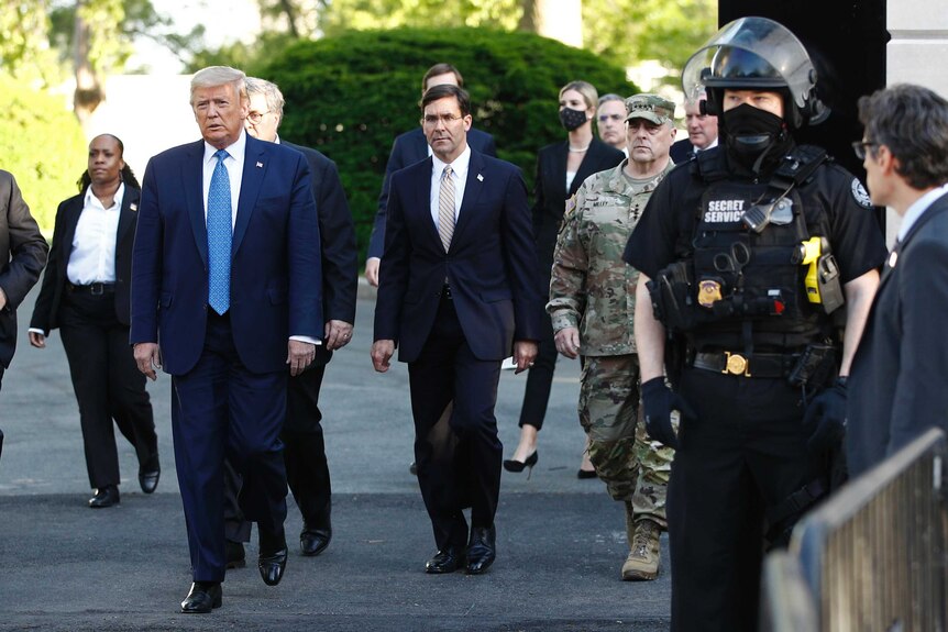 Donald Trump walks through a park, flanked by advisors and security