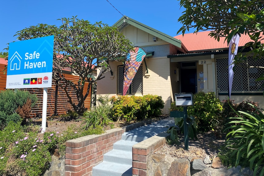 A cream coloured brick house with a large blue sign in the garden reading "Safe Haven".