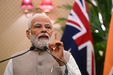 Narendra Modi raises his finger as he talks into microphones with flags behind him