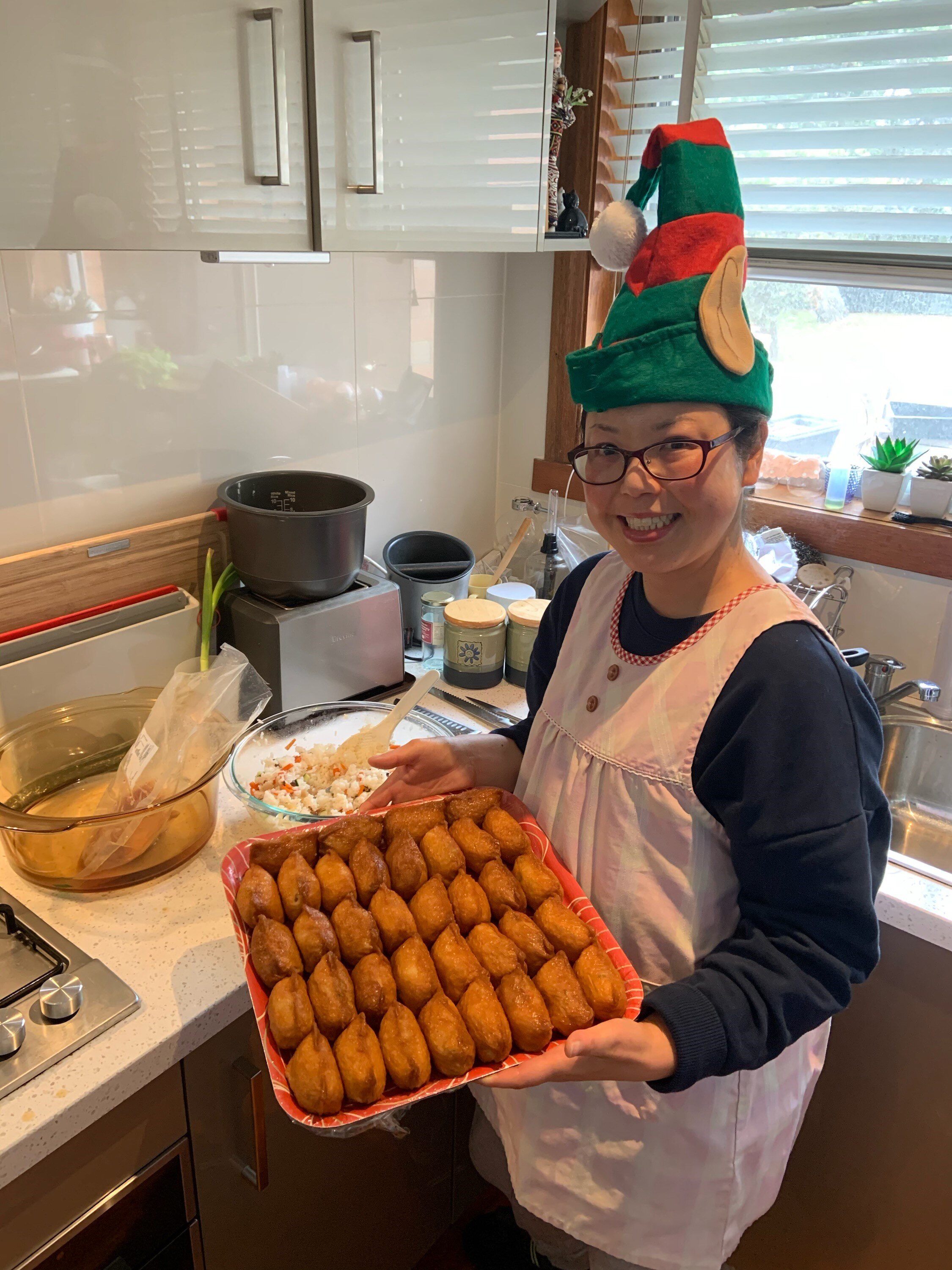 A woman wearing an elf hat shows a tray of inari