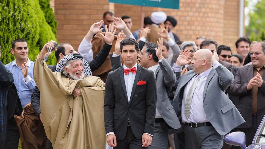 Family, holding their hands in the air in celebration, surround a young groom dressed in a suit.