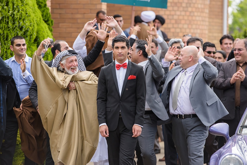 Family, holding their hands in the air in celebration, surround a young groom dressed in a suit.