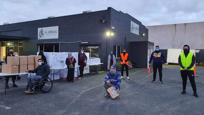 A group of people standing outside a grey building, all wearing masks.