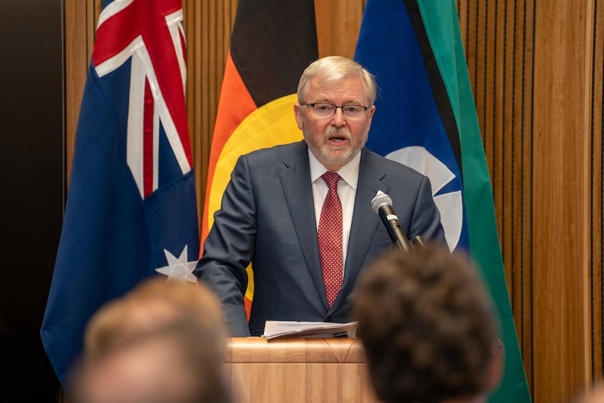 Kevin Rudd stands at a podium and speaks in front of Australian, Aboriginal and Torres Strait Island flags.