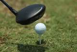 A driver hovers above a golf ball which sits on a tee
