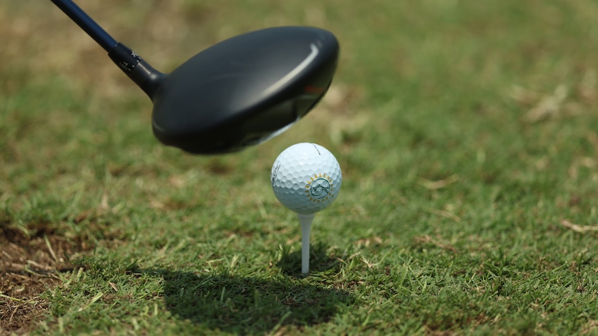 A driver hovers above a golf ball which sits on a tee