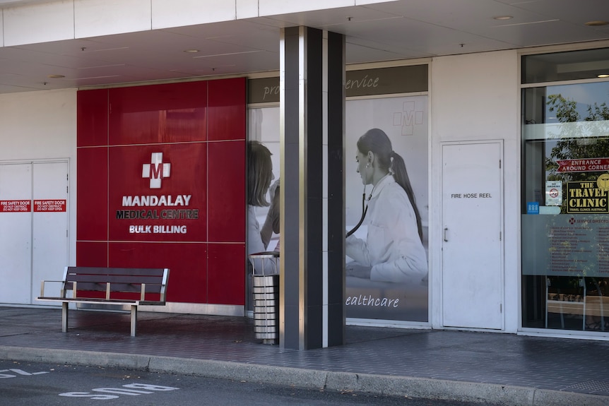 A red sign on a building reading 'Mandalay' in front of a seat and bin