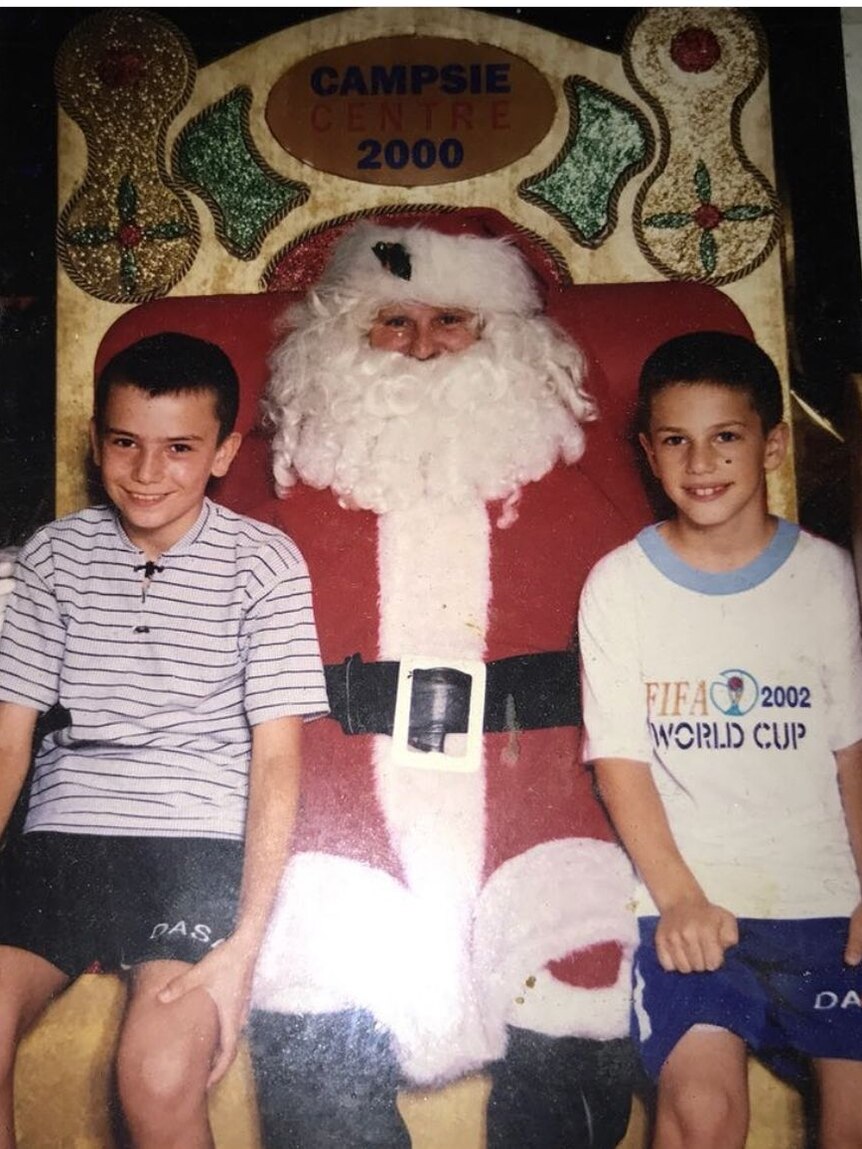 Two young boys pose for a photo with a shopping centre Santa Claus 