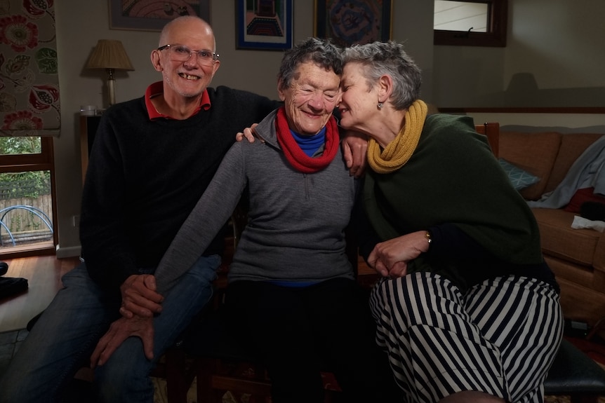 Two women and a man sit with their arms around each other