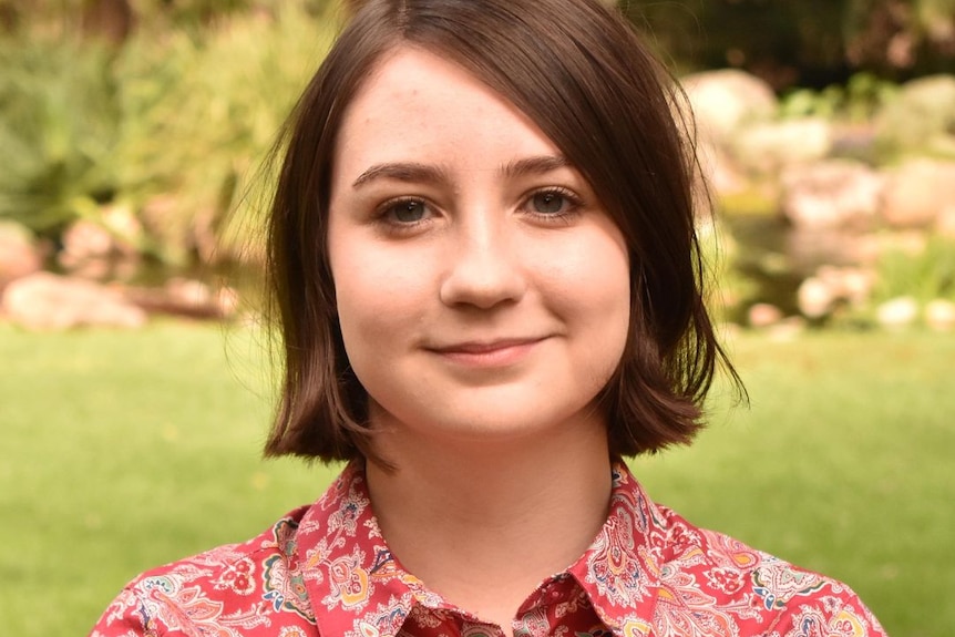 A young woman in a bright button up shirt stands with her arms crossed.