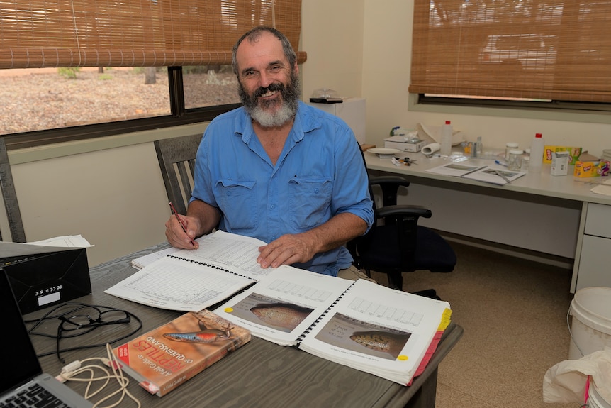 A man with a beard in a blue shirt sitting at a desk looking at pictures and notes on yakka skinks
