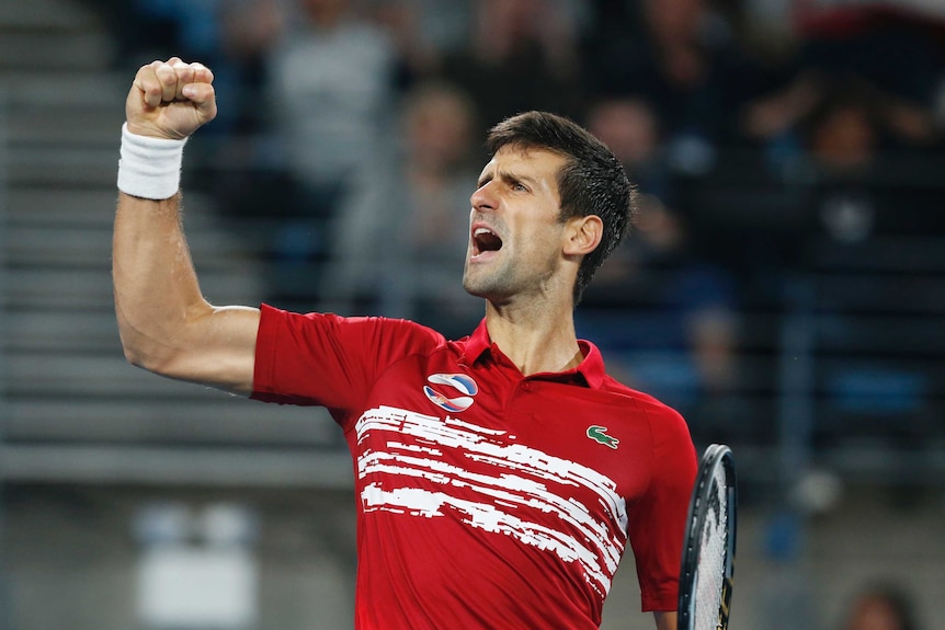 A tennis player punches his fist in celebration after winning a point in a teams tournament match.