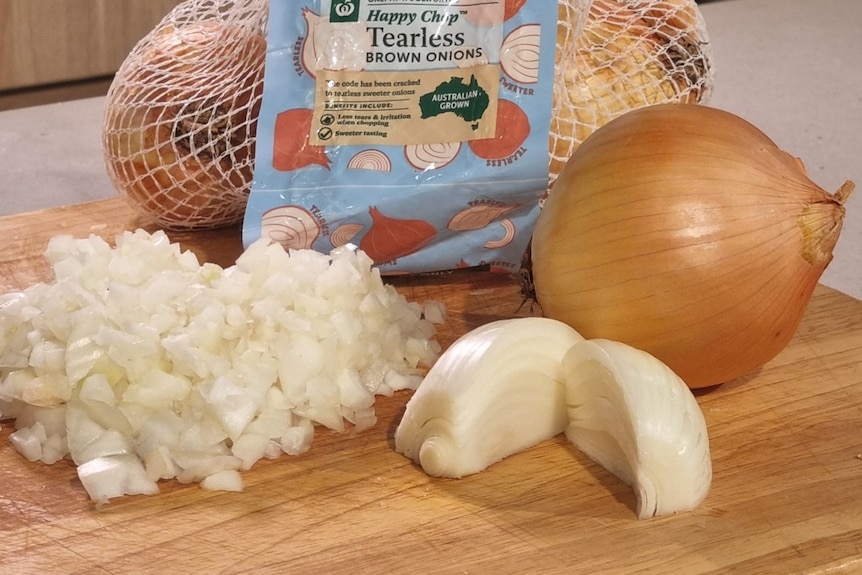 A cutting board with half cup onions, chopped onions and a branded bag of onions. 