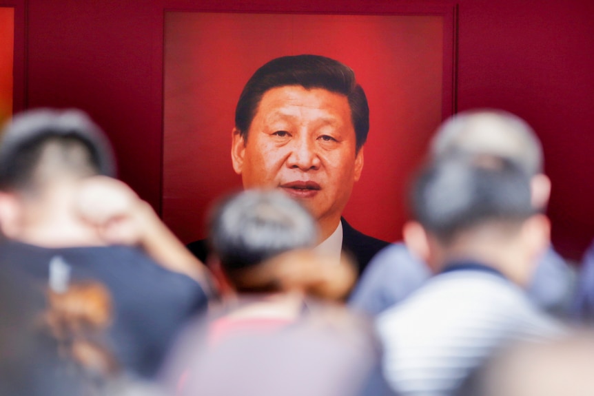 A crowd of people looking at a poster of Xi Jinping 