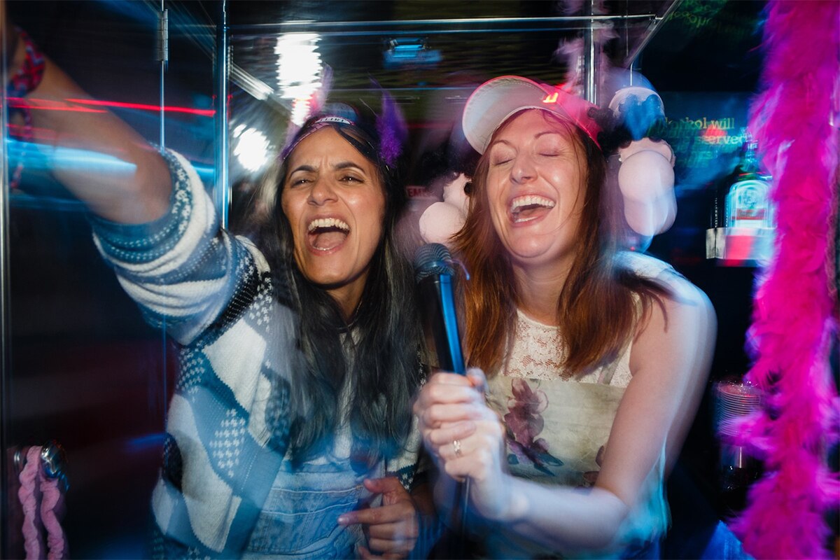 Colour still from 2018 film The Breaker Upperers of actors Madeleine Sami and Celia Pacquola singing karaoke in a night club.