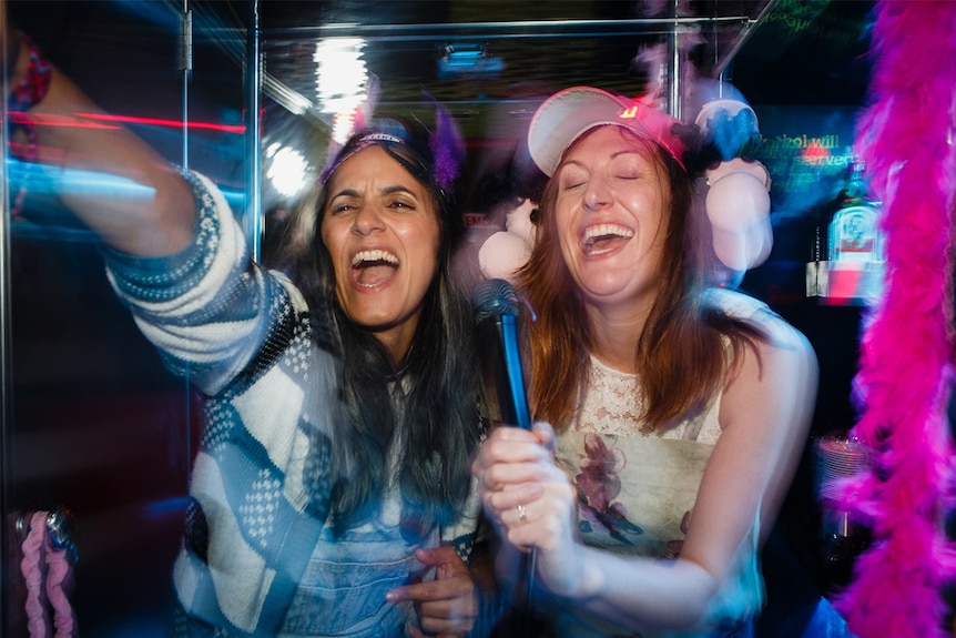 Colour still from 2018 film The Breaker Upperers of actors Madeleine Sami and Celia Pacquola singing karaoke in a night club.