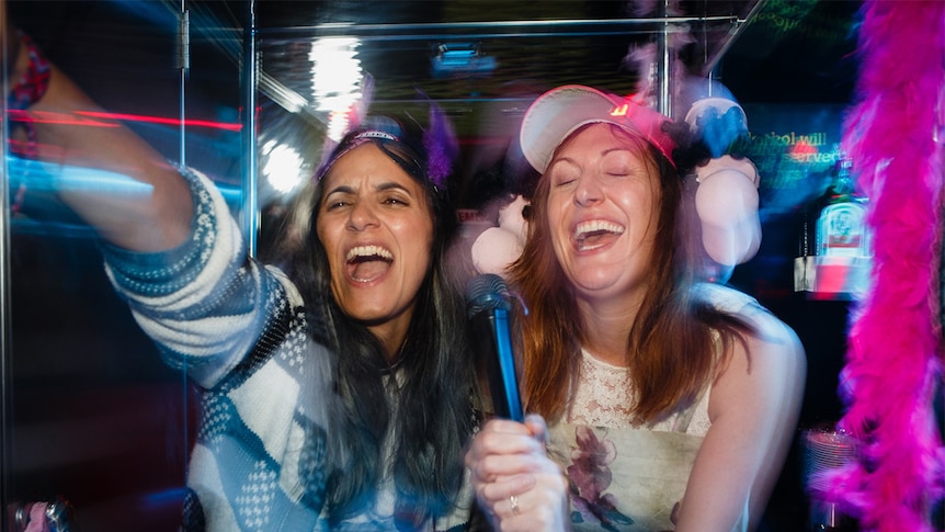 Colour still from 2018 film The Breaker Upperers of actors Madeleine Sami and Celia Pacquola singing karaoke in a night club.