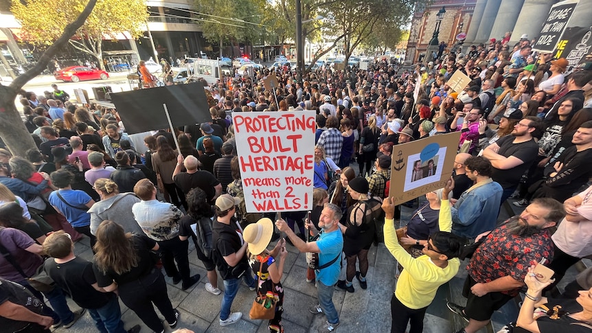 crowd of people hold placards facing a busy city street
