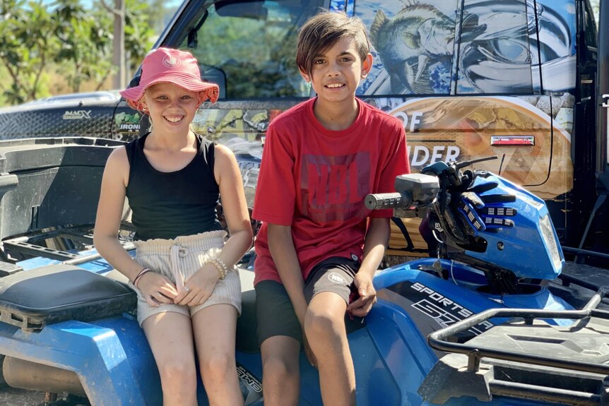 Two children smiling on a quad bike.