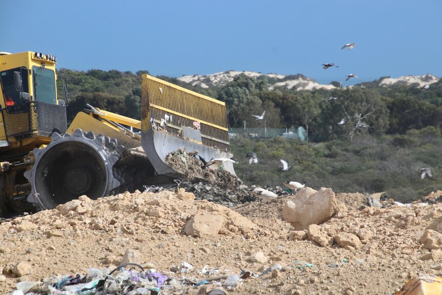 A close-up of a yellow bulldozer pushing rubbish into a pile at a landfill site.