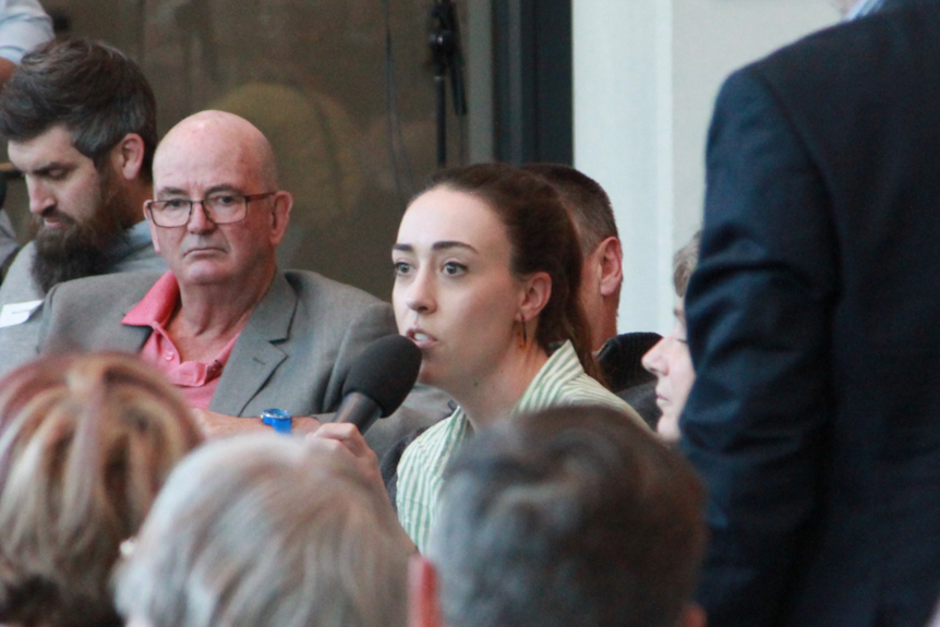 Zoe holds a microphone and asks a question to the panel.