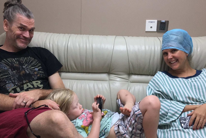 Man and woman smiling on a couch with a child lying between them