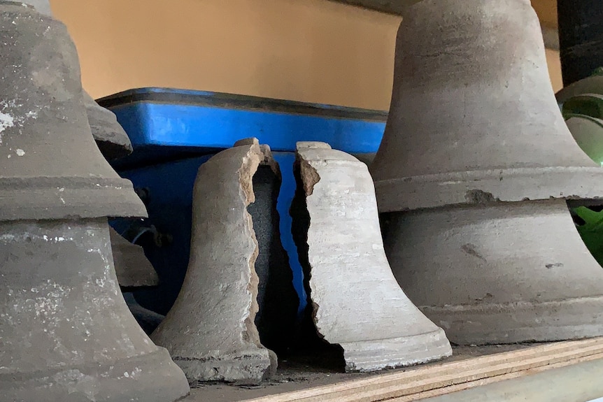 grey moulds in the shape of bells on shelving, middle one is broken showing a bell was removed from the cast