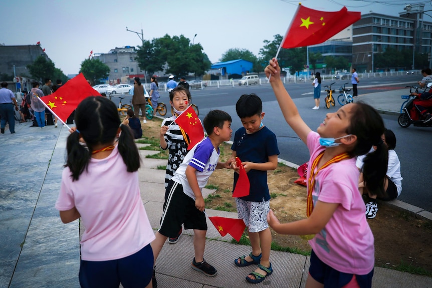 Small children waving Chinese flags, with masks pulled down below their chins 