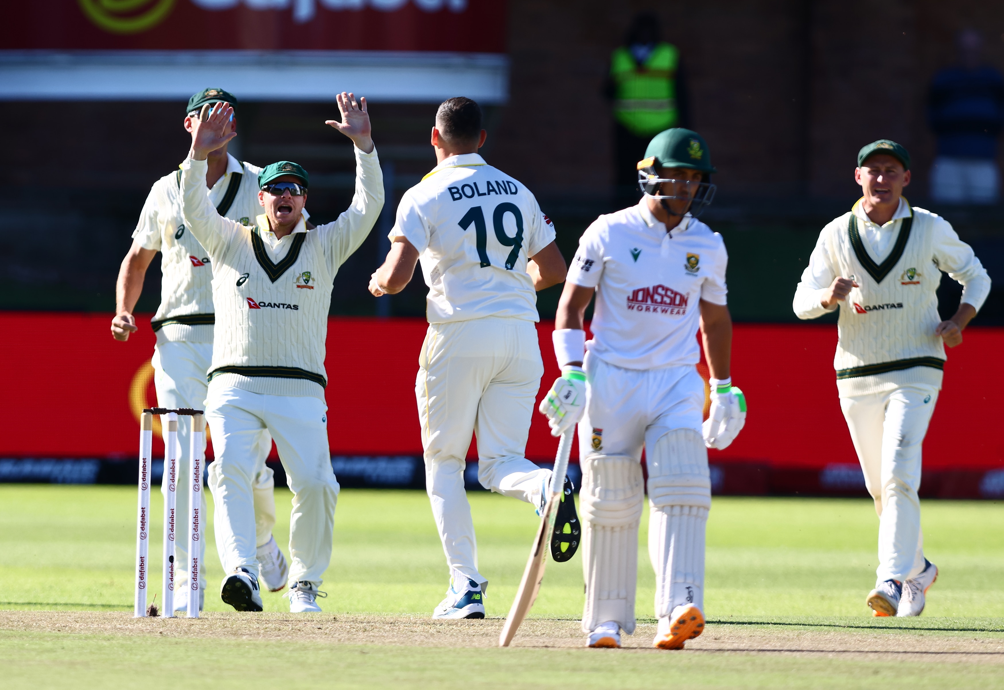 A cricket batter walks from the middle as a group of teammates celebrate behind him