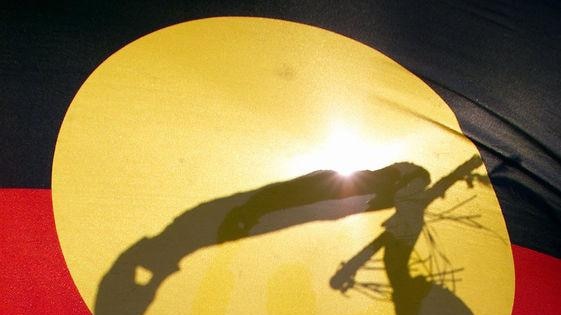 An Aboriginal elder silhouetted behind the Aboriginal flag.