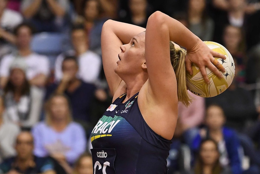 A female netball player holds the ball behind her head as she prepares to shoot for goal.