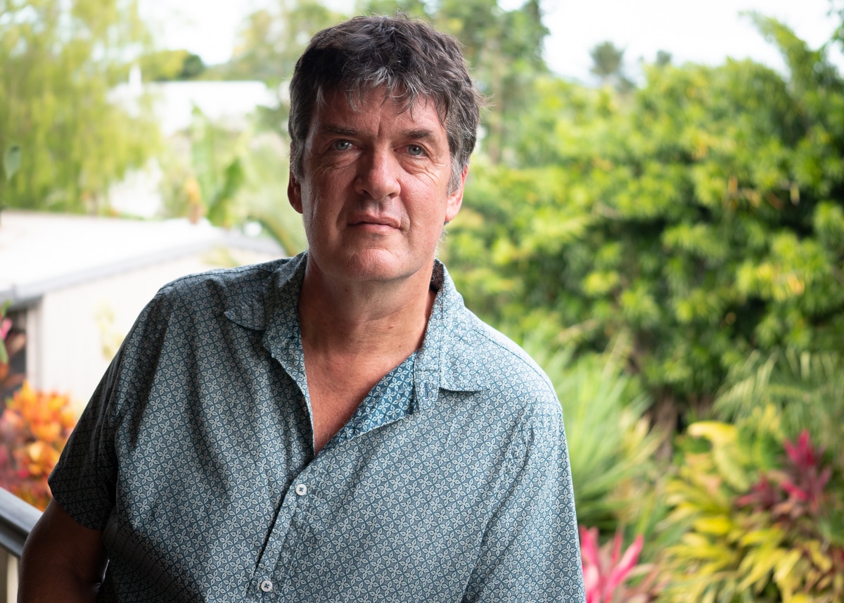 Man wearing a teal button up shirt standing outside.
