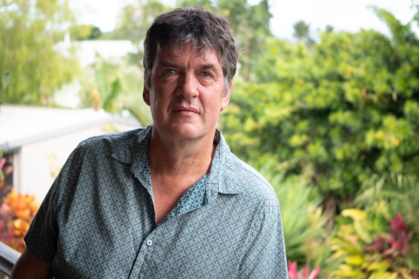 Man wearing a teal button up shirt standing outside.