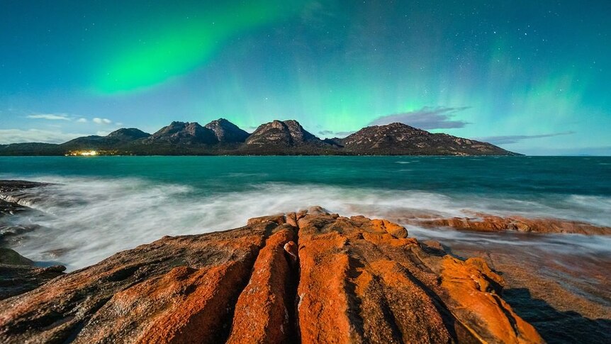 Aurora Australis over some mountains and the ocean.