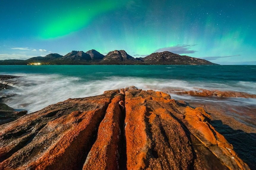 Aurora Australis over some mountains and the ocean.