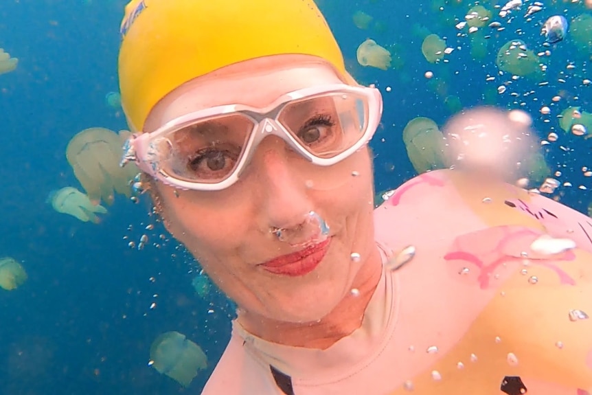 A woman with a bright yellow swimming cap with jellyfish in the water