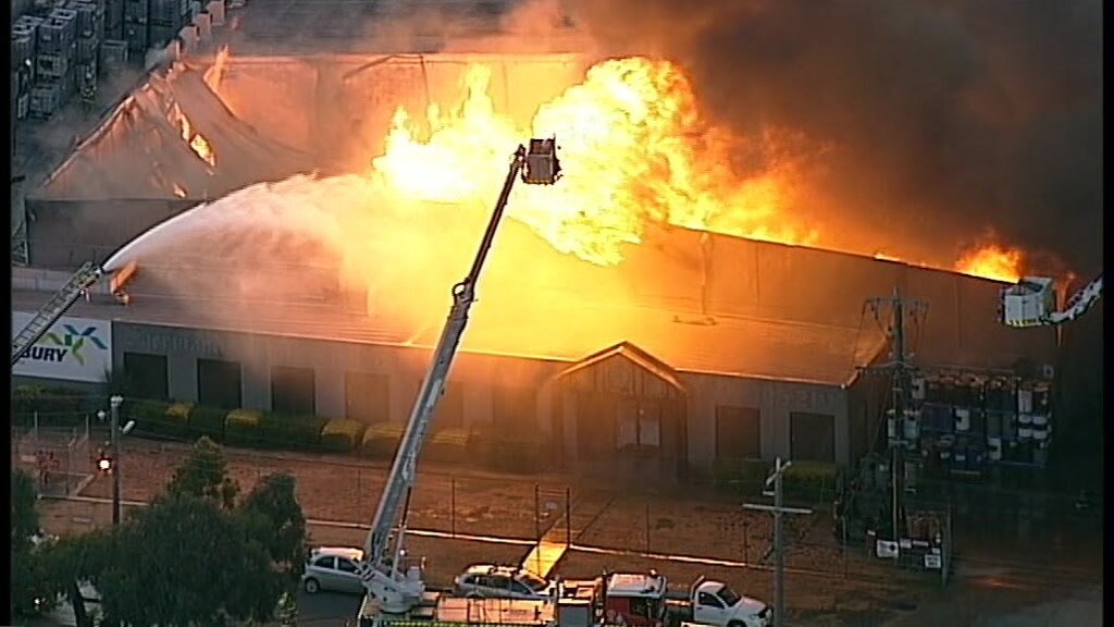 Flames engulf a large factory as fire crews battle to douse the flames from above.
