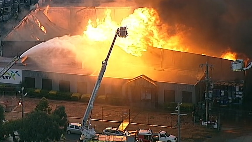 Flames engulf a large factory as fire crews battle to douse the flames from above.