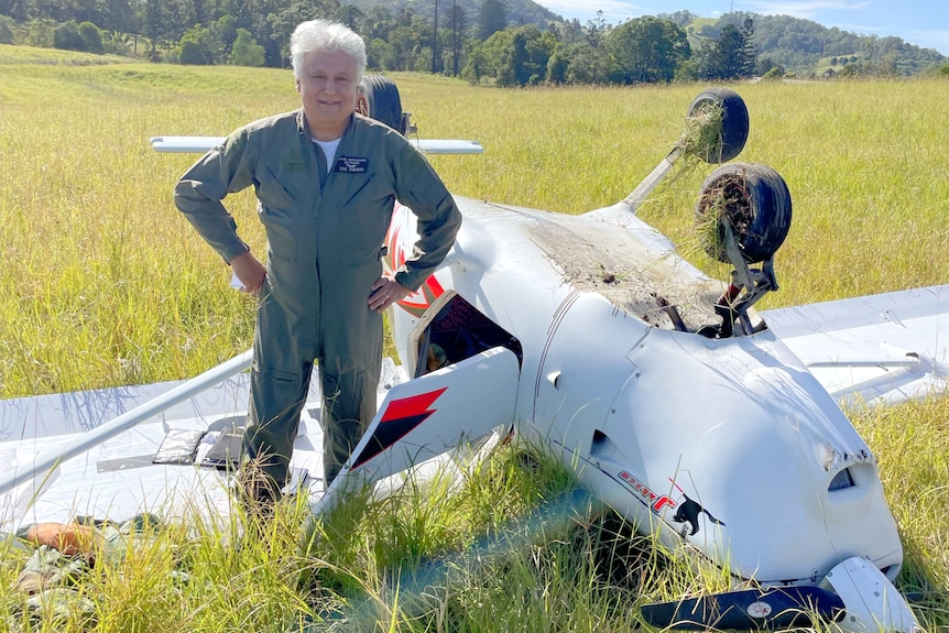 A man stands beside an upturned plane in a paddock.